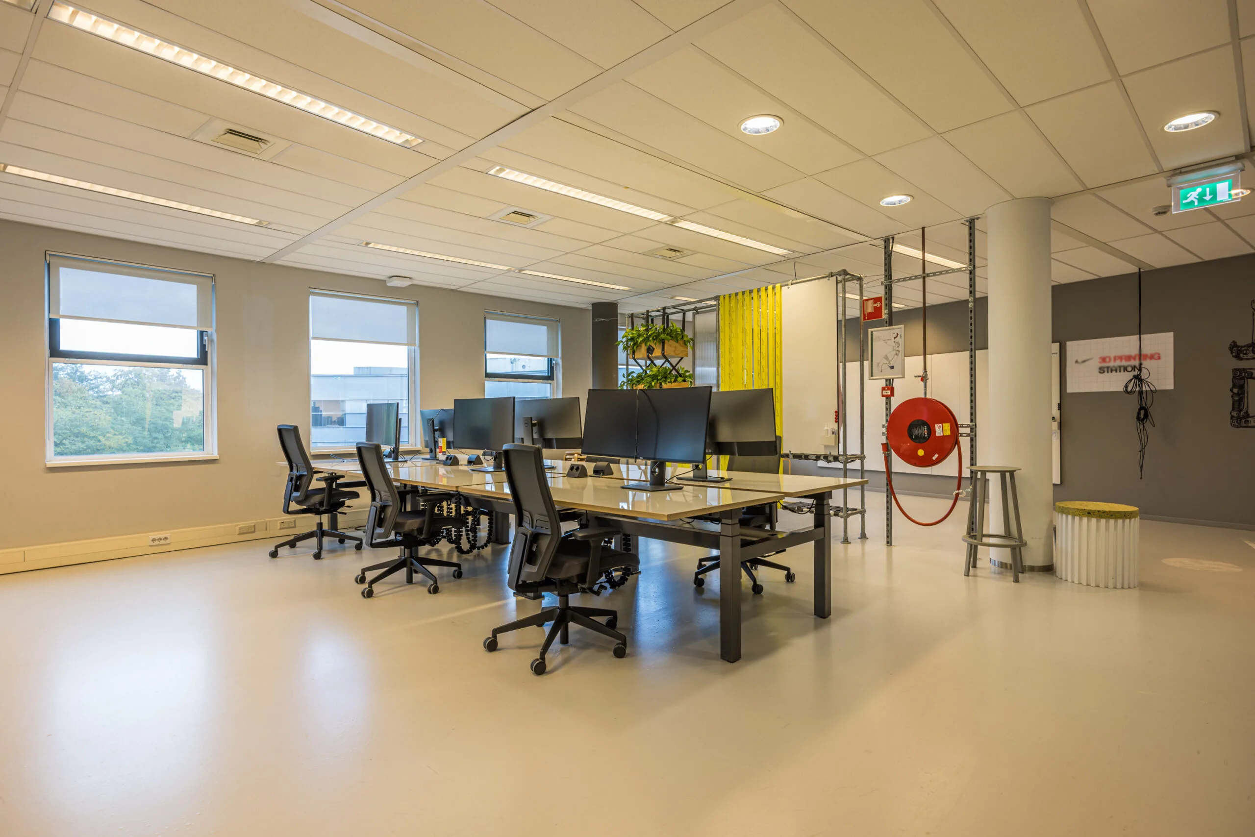Modern open-plan office space with multiple workstations, ergonomic chairs, and large monitors, located in the Olympia building.