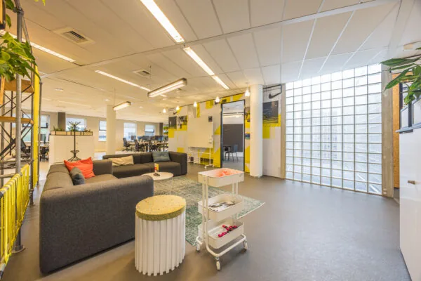 Modern office lounge area at Olympia featuring a gray sectional sofa, colorful accents, and large glass block windows.