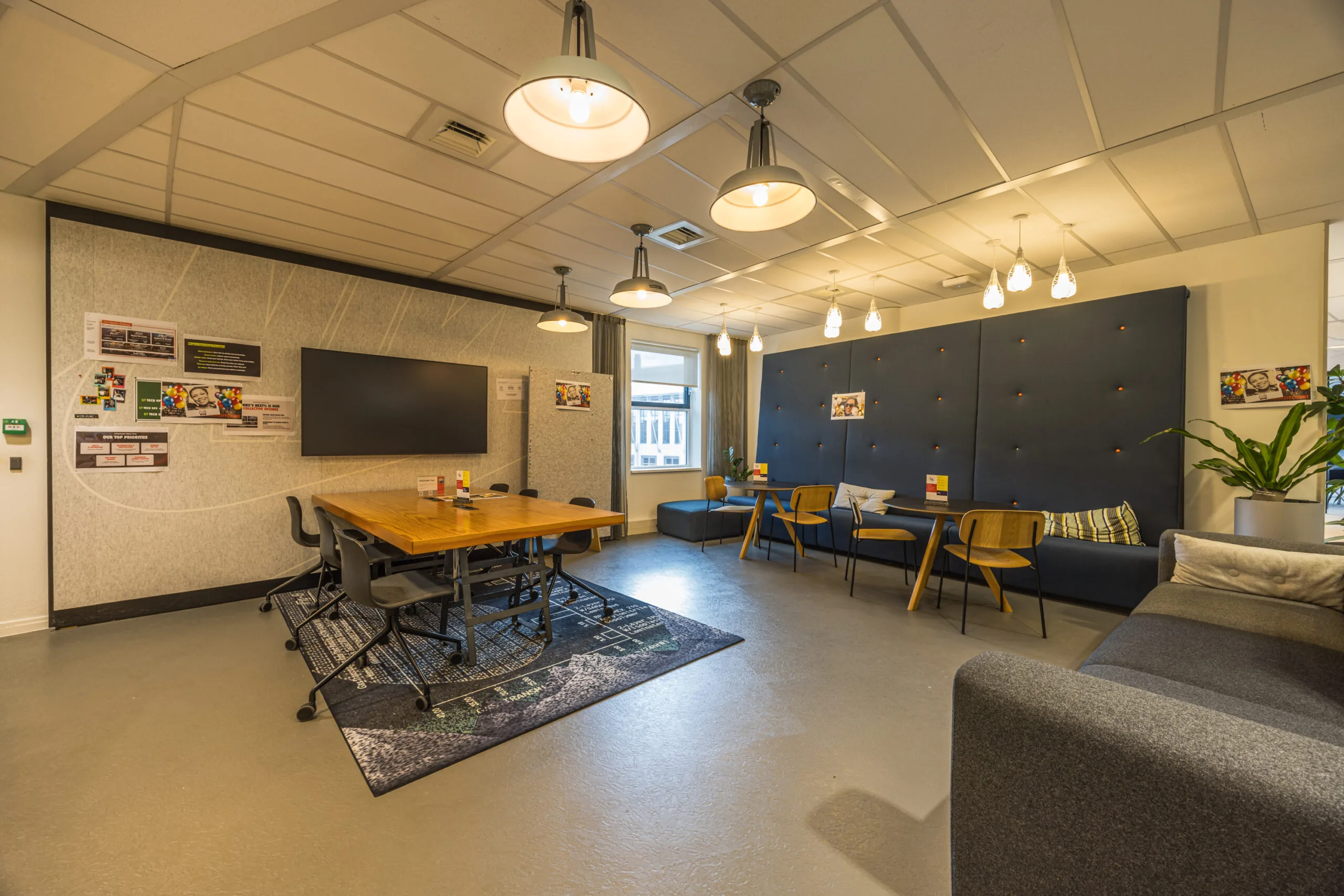 Modern office lounge with a meeting table, cozy seating areas, and warm lighting.