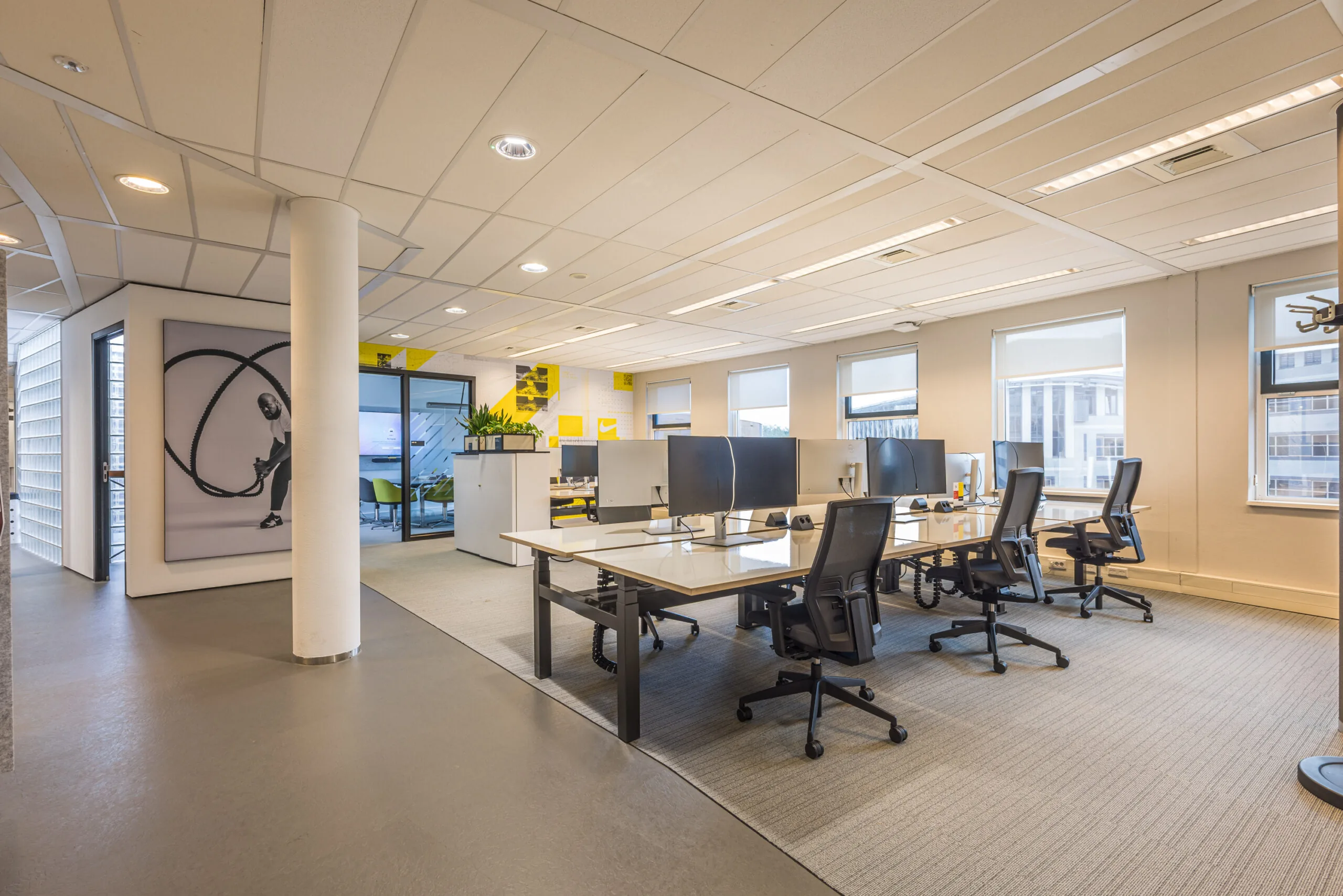 Modern open-plan office space at Olympia with workstations, ergonomic chairs, and a large fitness-themed wall art.