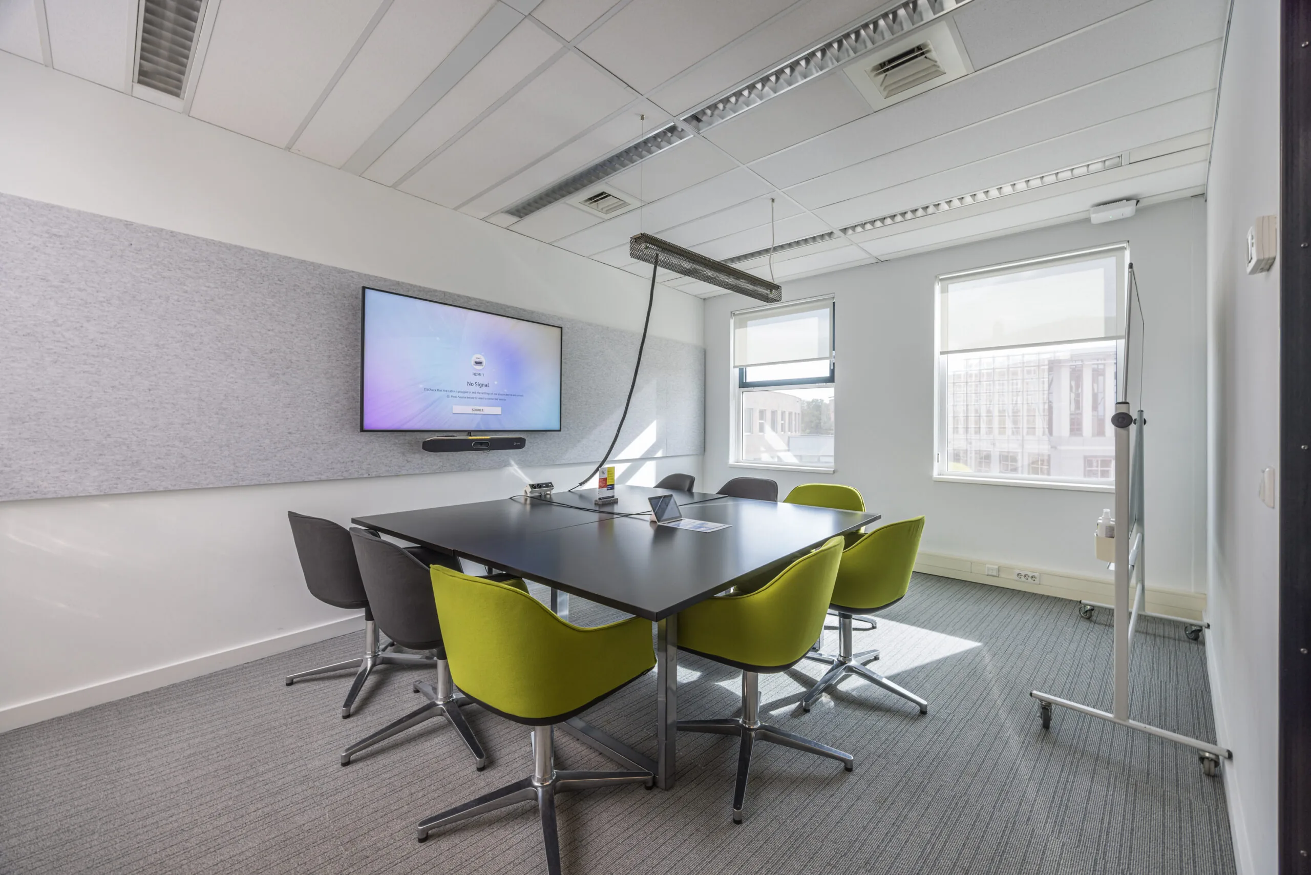 Modern meeting room at Olympia featuring a large screen, conference table, and colorful chairs.