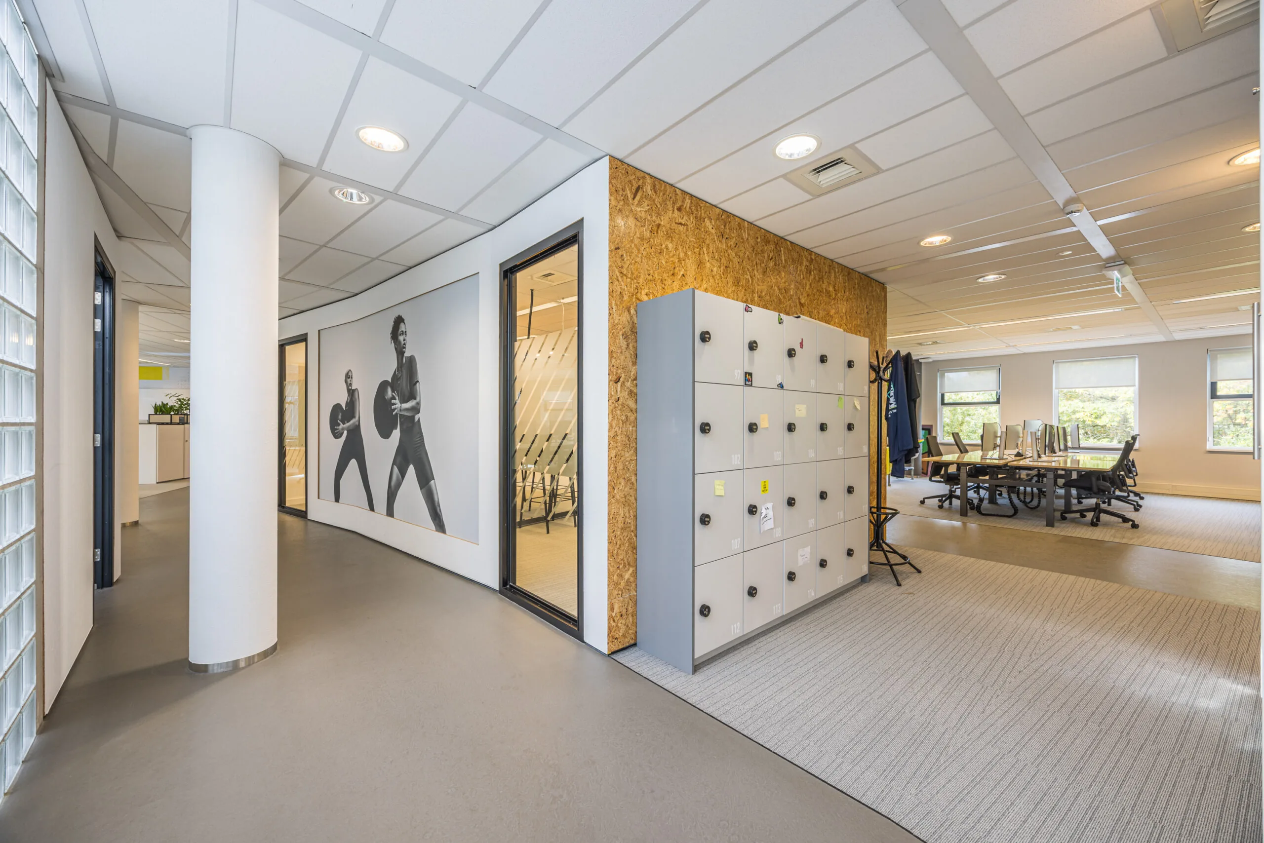 Modern office interior with lockers, a meeting area, and a wall mural of people exercising.