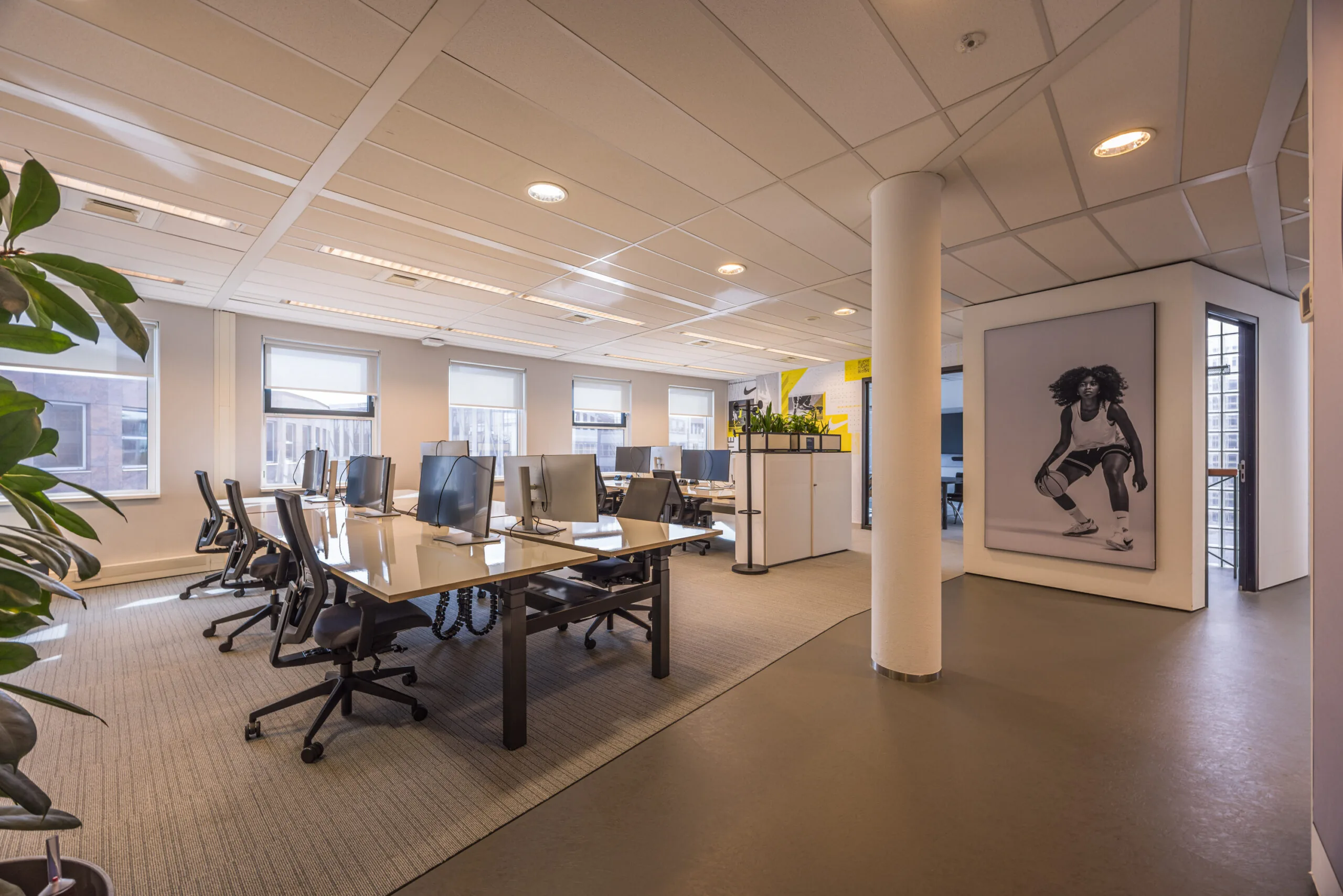 Modern open-plan office space with multiple desks, computers, and a large black-and-white sports-themed wall art featuring an athlete.