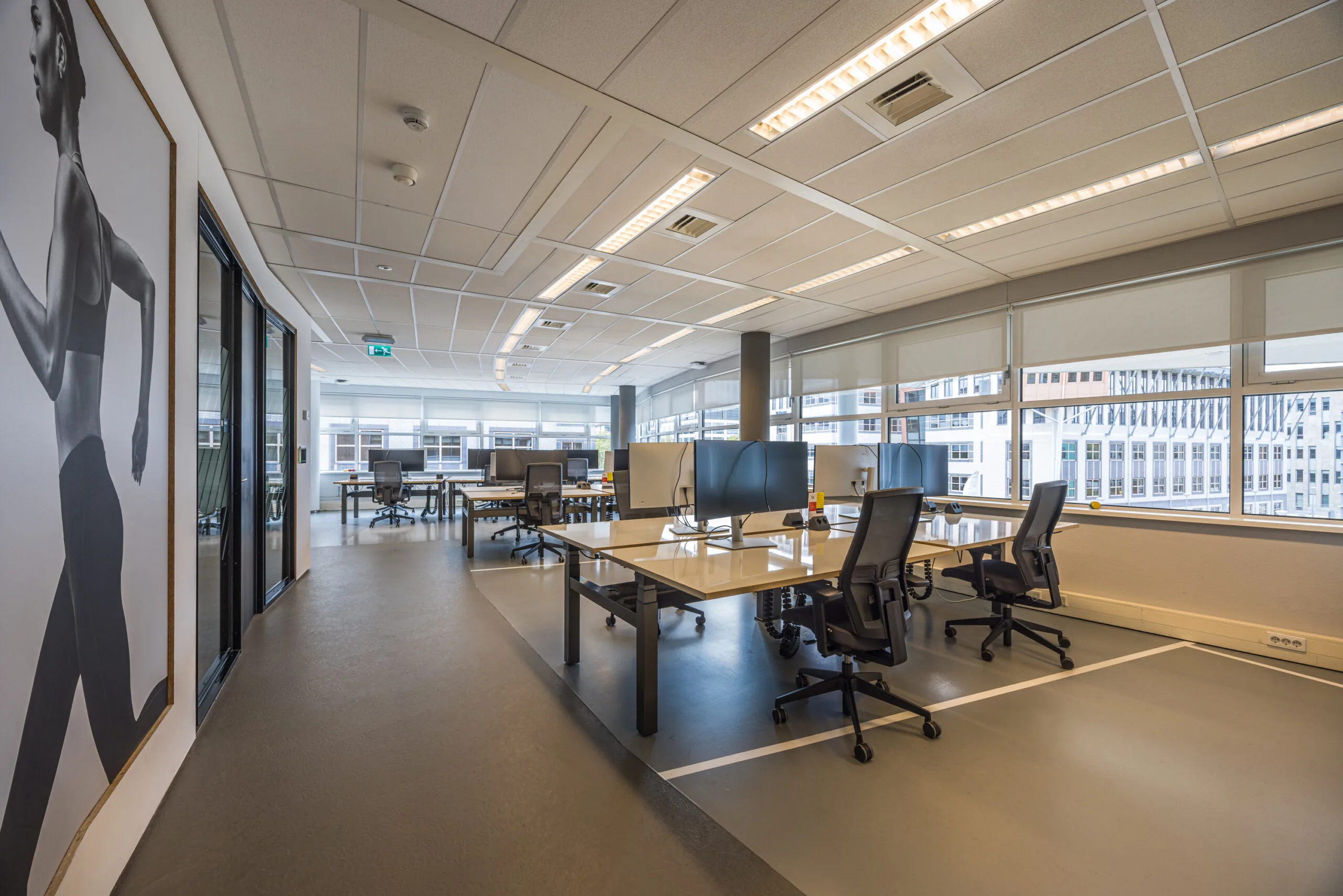 Modern open-plan office space with multiple workstations, large windows, and a wall-sized photo of a runner.