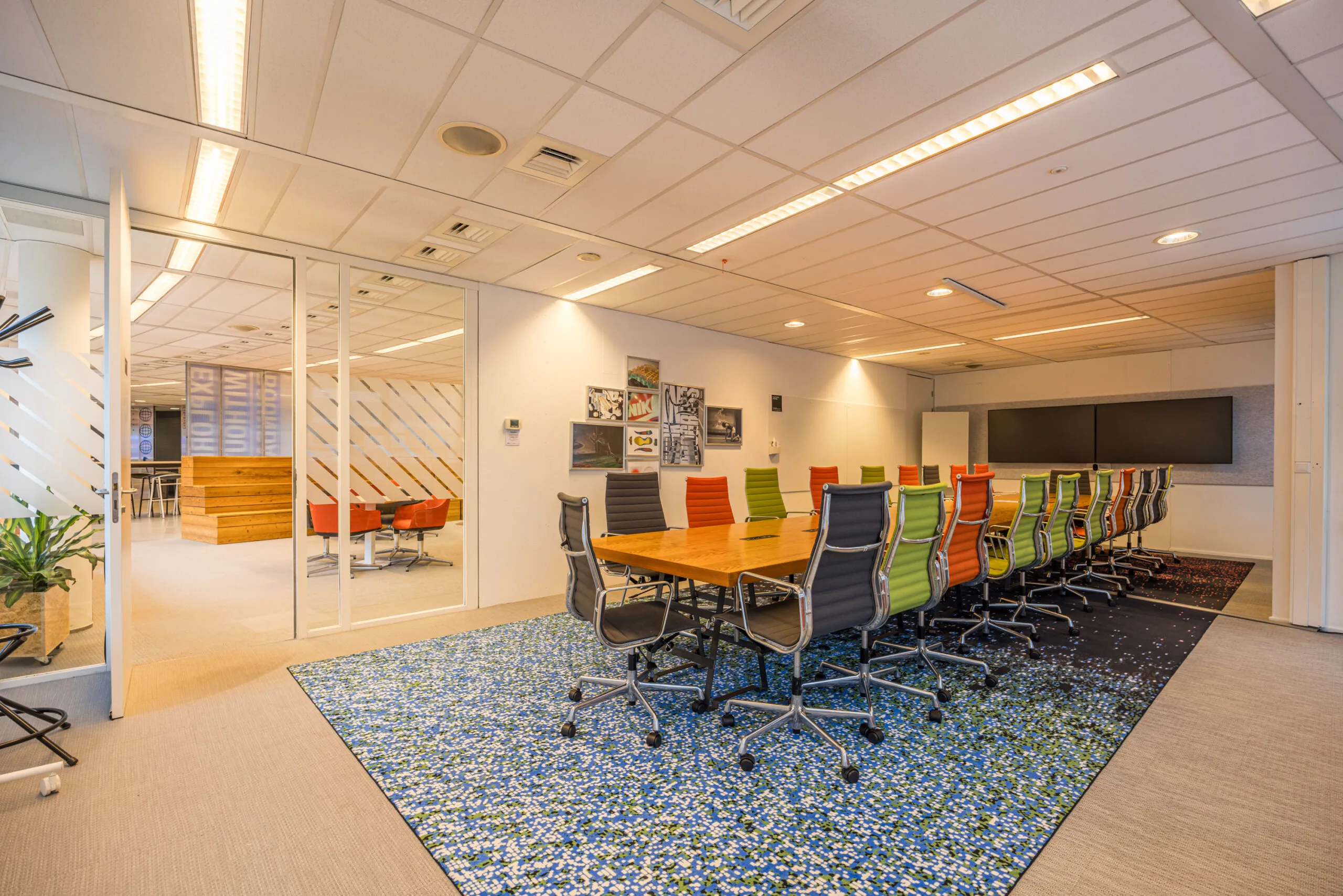Modern conference room at Olympia with colorful chairs, a long wooden table, and wall-mounted screens.
