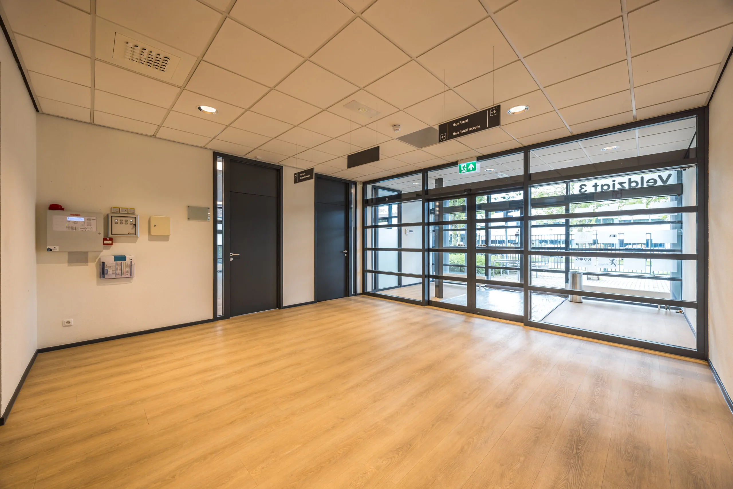 Modern entrance hall with wooden flooring, black doors, and large glass windows at Veldzigt 3.