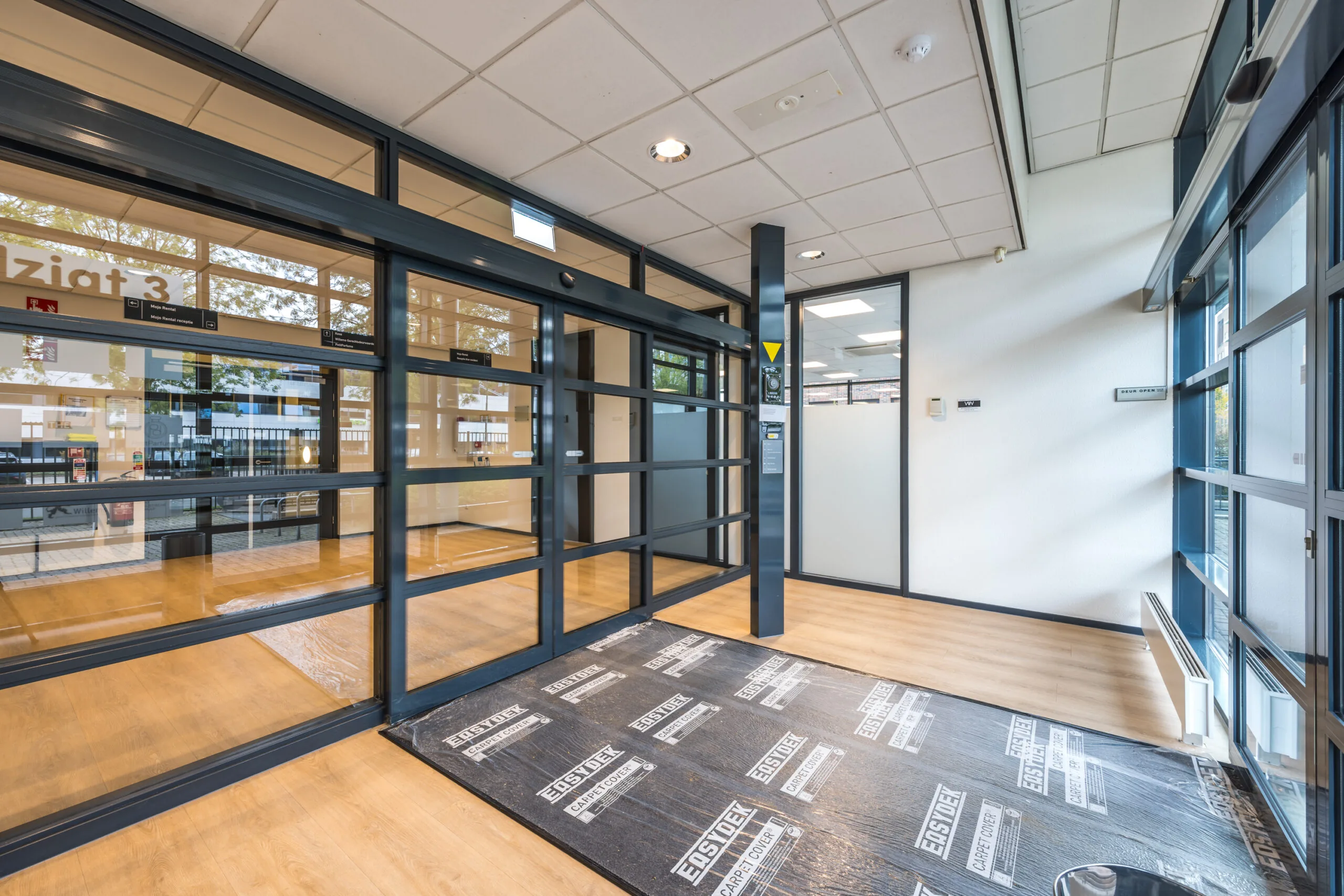 Modern office entrance with glass walls and automatic sliding doors at Veldzigt 3.