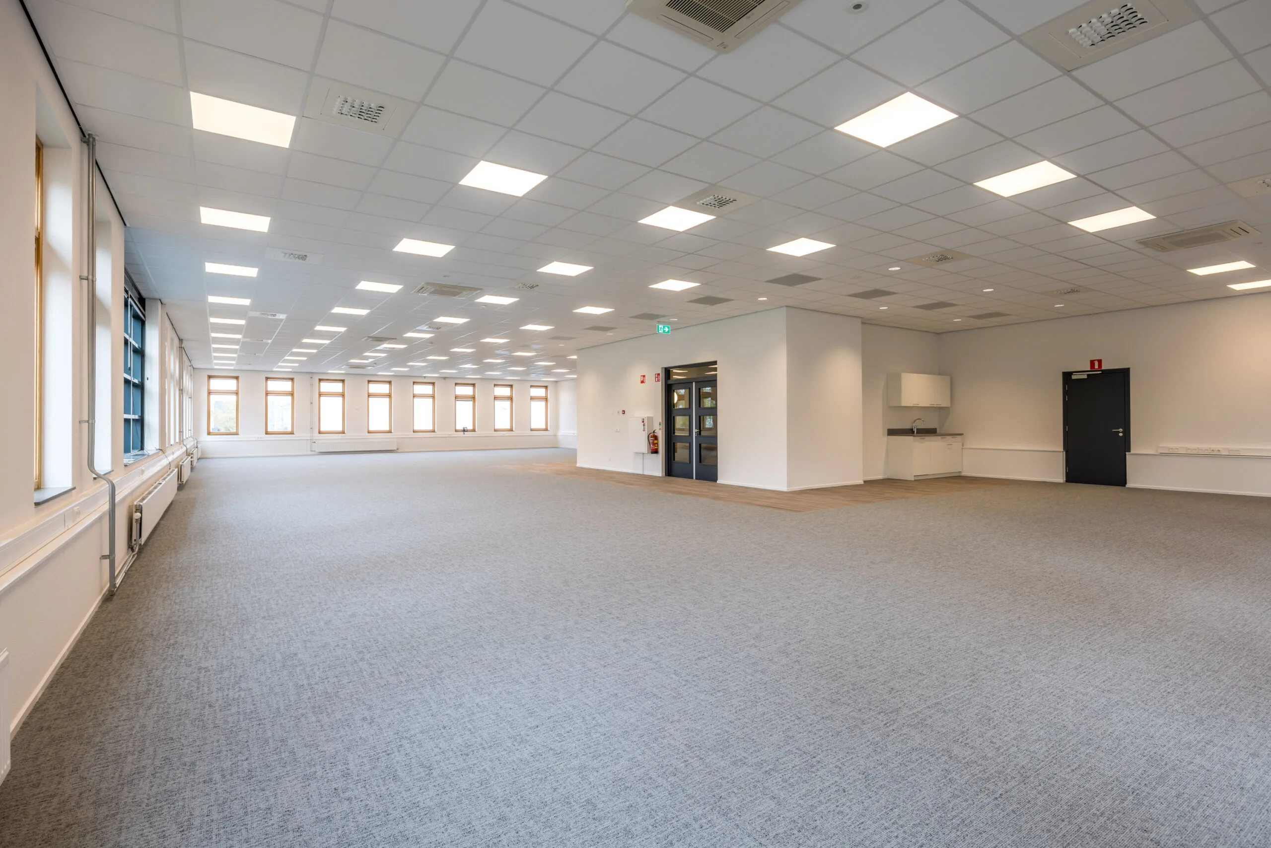 Spacious empty office space at Veldzigt with carpeted floors, large windows, and a suspended ceiling with integrated lighting.