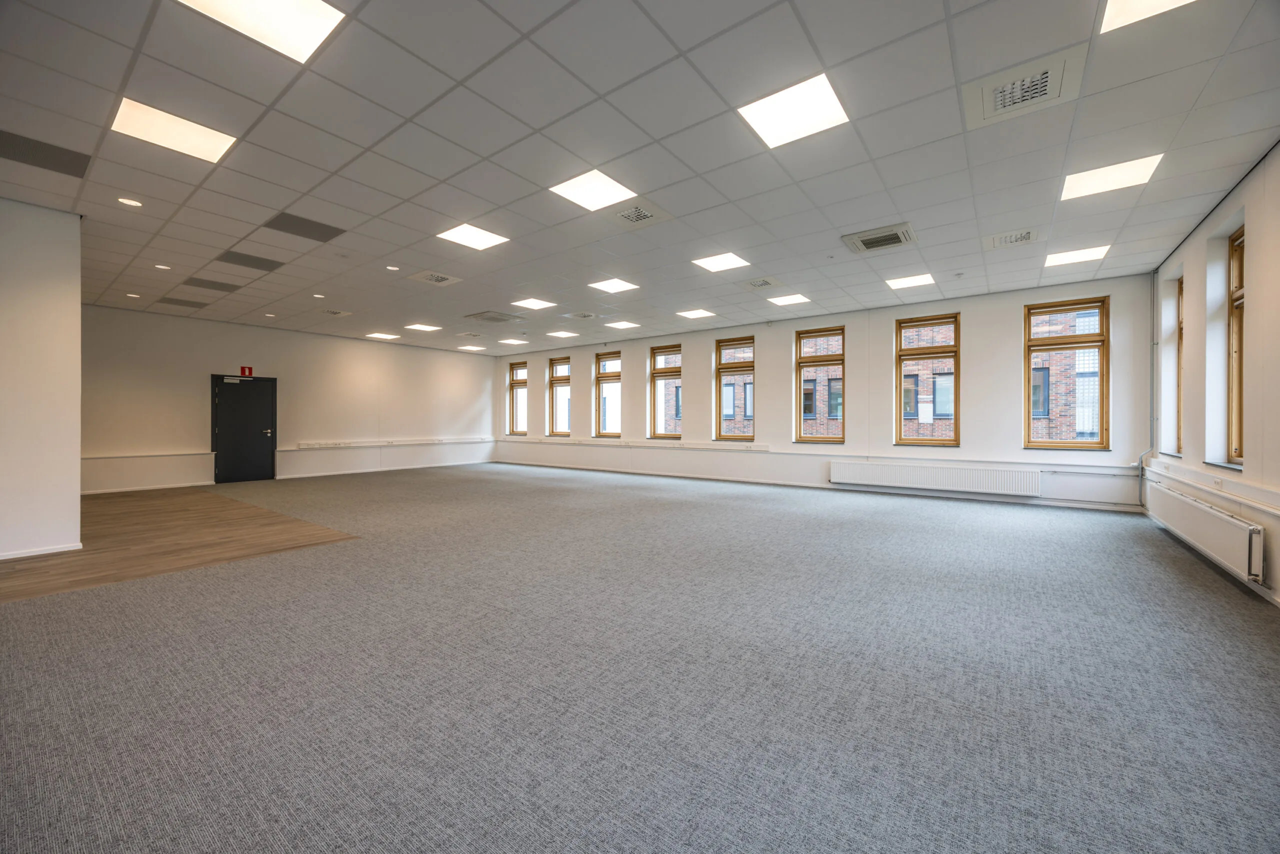 Spacious and brightly lit empty office space with carpeted flooring and large windows at Veldzigt.