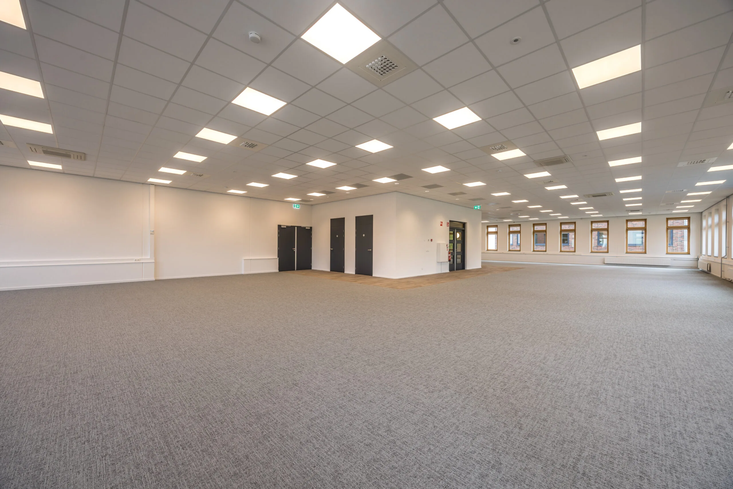 Spacious, modern office space with carpeted flooring, white walls, and large windows at Veldzigt.