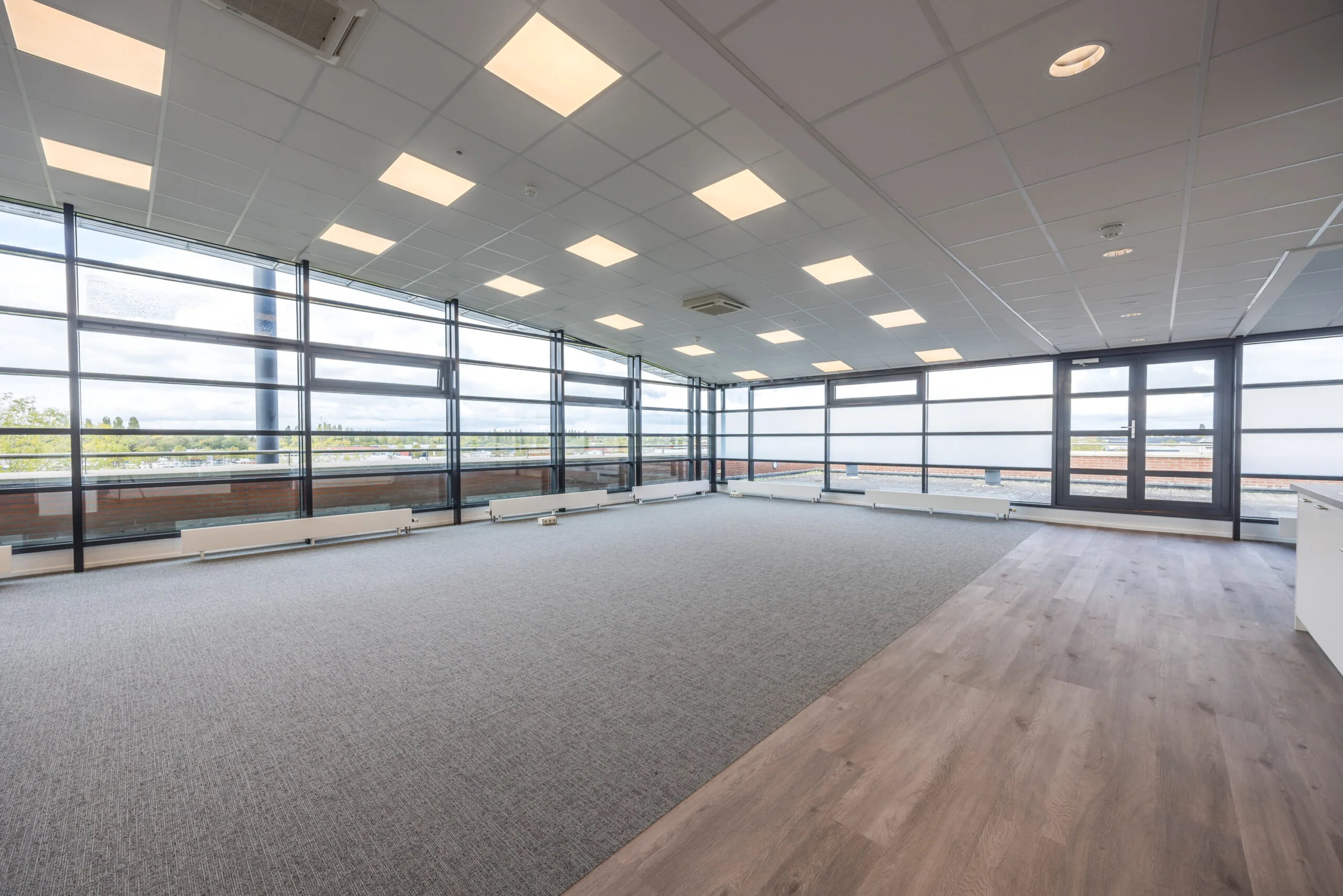 Bright, spacious office space at Veldzigt with large windows, carpeted floor, and modern ceiling lighting.