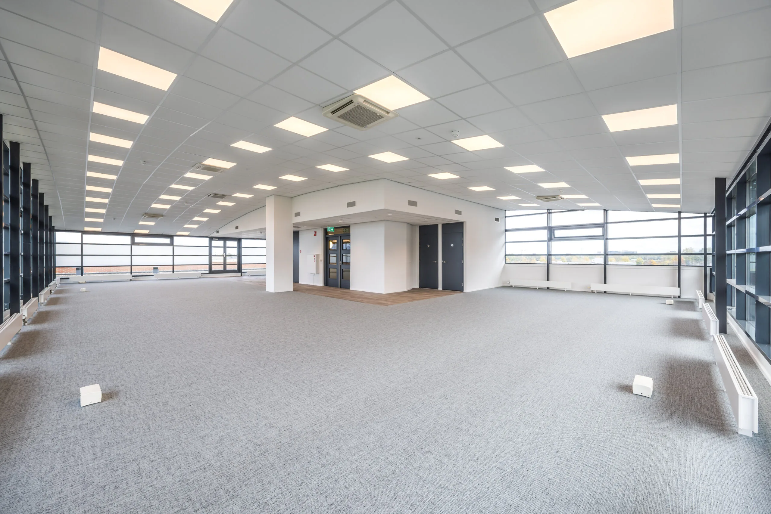 Spacious modern office space at Veldzigt with large windows, carpeted floor, and ceiling lights.