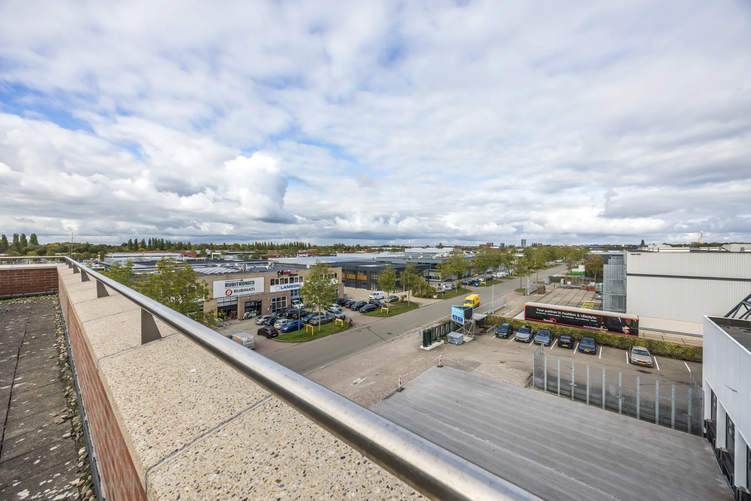 View over the Veldzigt industrial area with commercial buildings, parked cars, and a partly cloudy sky.