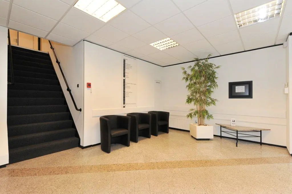 Modern waiting area at Oosteinde 176, featuring black chairs, a potted plant, and a staircase.