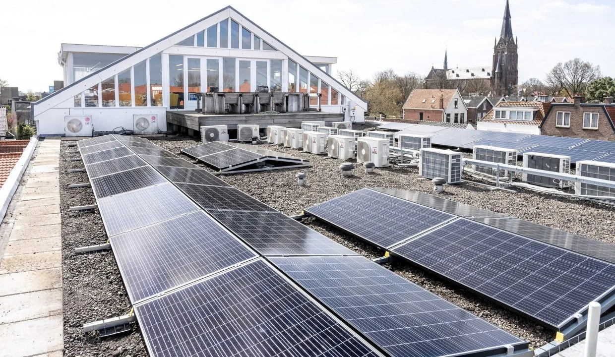 Rooftop solar panels and HVAC units on a commercial building at Oosteinde with a church visible in the background.