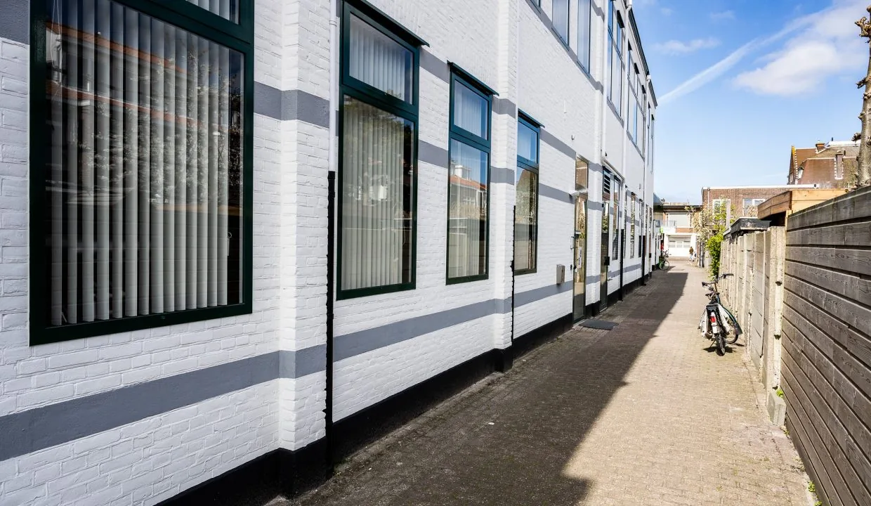 Narrow alleyway beside a white brick building with striped gray accents on Oosteinde street.