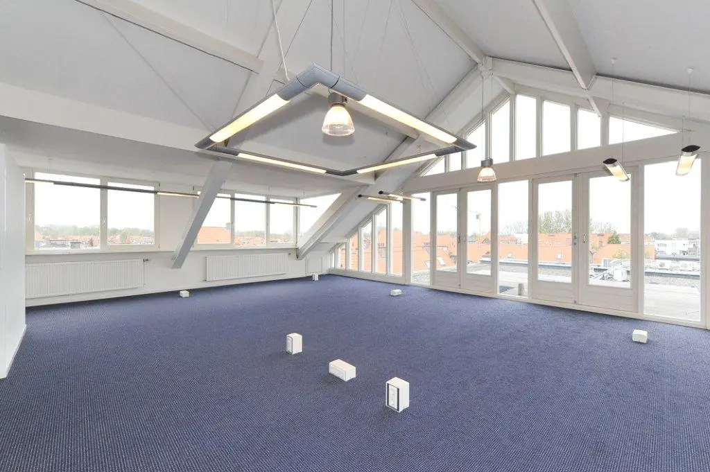 Bright, empty office space at Oosteinde with large windows, modern lighting, and blue carpet flooring.