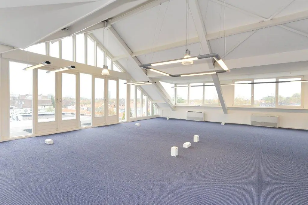Spacious, modern office space at Oosteinde with large windows, blue carpet, and exposed ceiling beams.