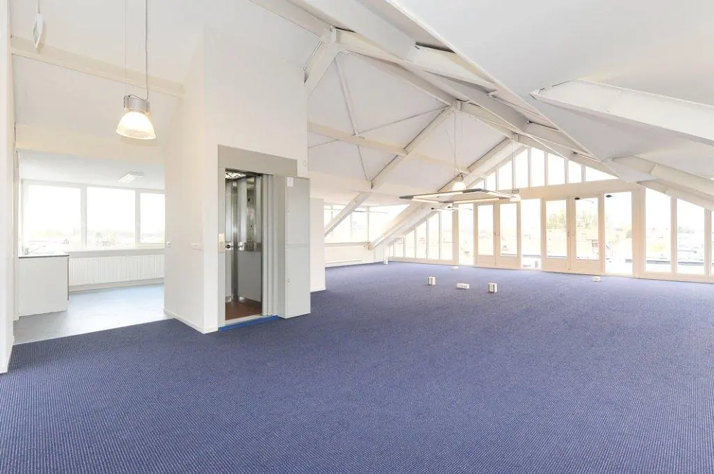 Spacious modern office interior at Oosteinde with high ceilings, blue carpet, large windows, and an elevator.