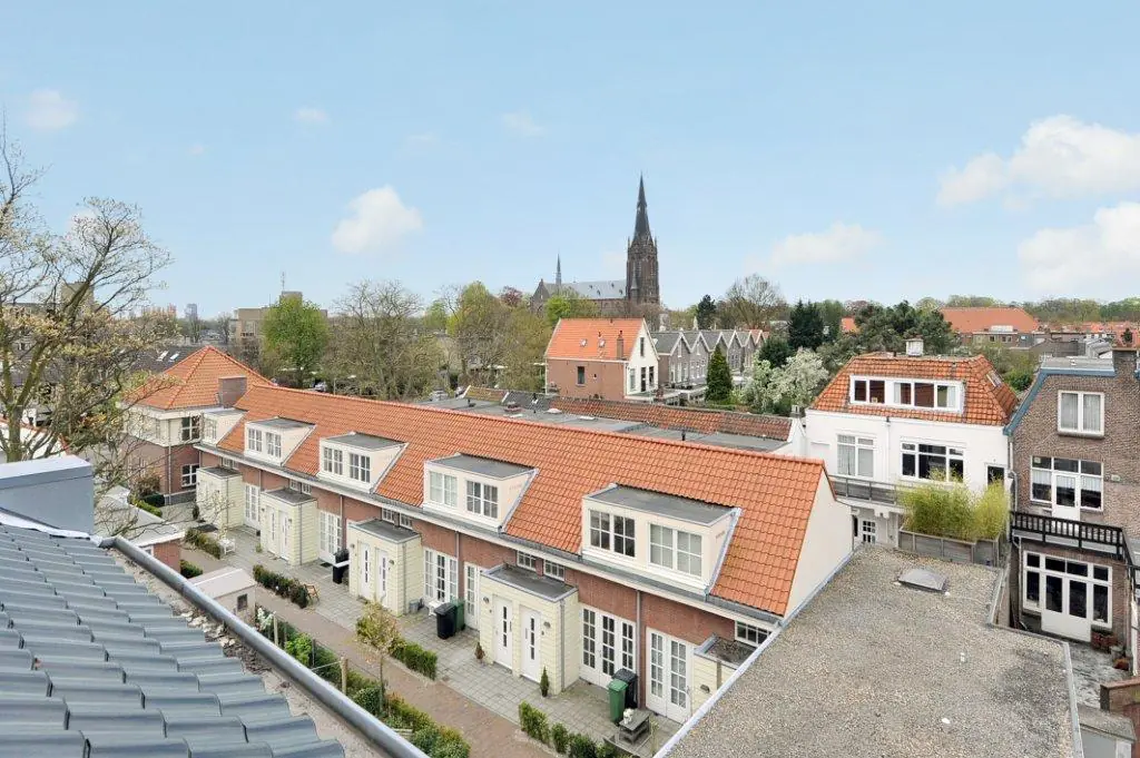 View over a row of Dutch townhouses with red tiled roofs in Oosteinde, featuring a church tower in the background.