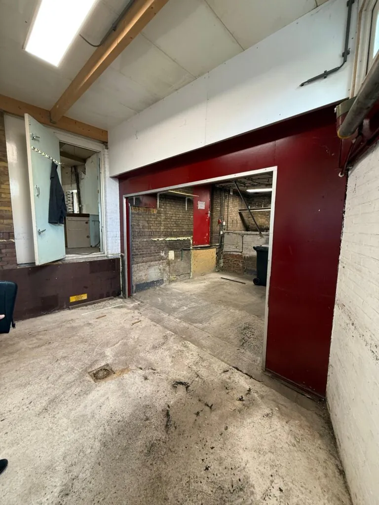 Binnenruimte van een verouderd gebouw aan de Prinses Mariannelaan met betonnen vloer en deels gesloopte muur.