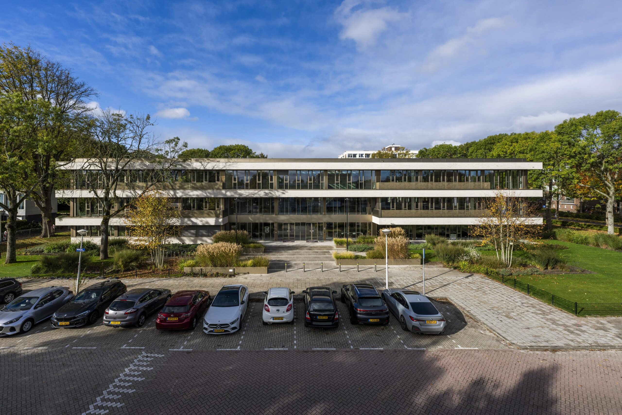 Modern office building "Walborg" with a parking lot in front, surrounded by trees and greenery under a partly cloudy sky.