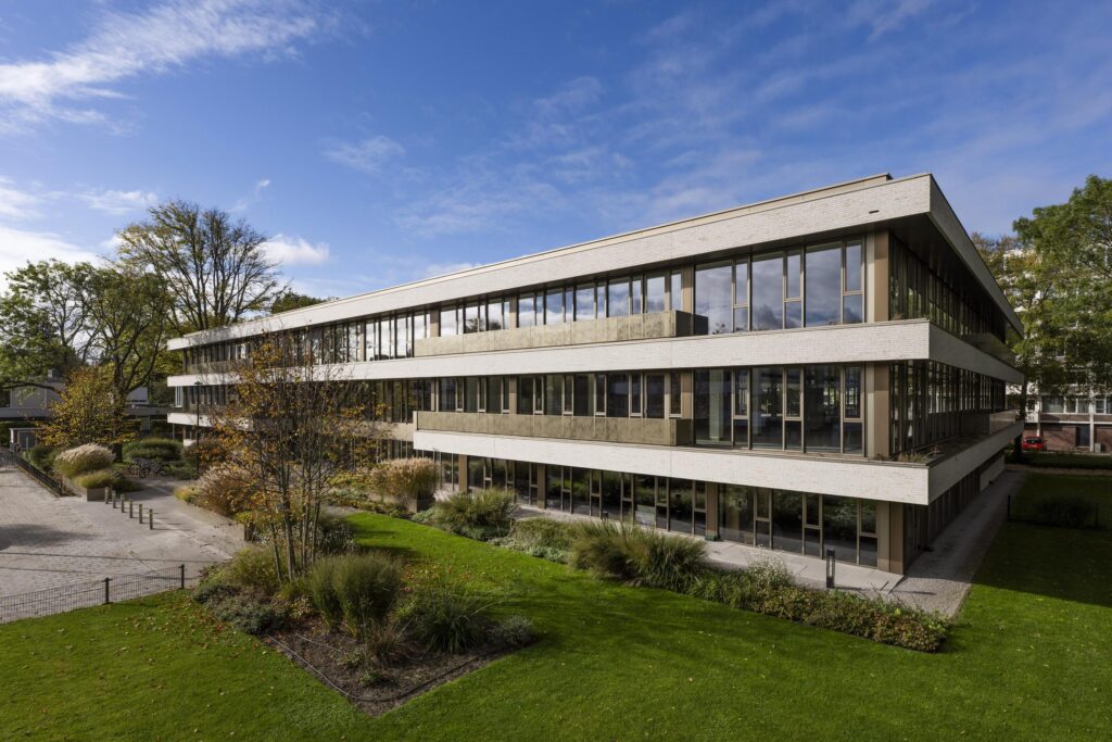 Modern three-story Walborg office building with large windows, surrounded by greenery and trees under a partly cloudy sky.