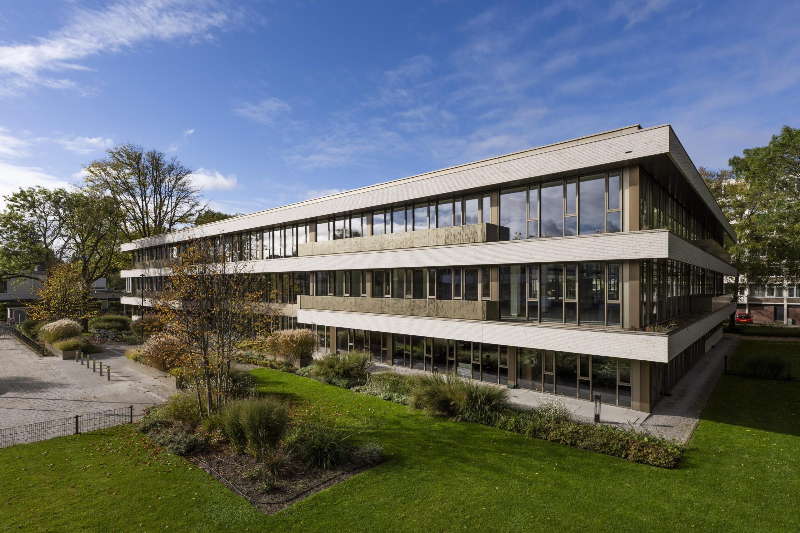 Modern three-story Walborg office building with large windows, surrounded by greenery and trees under a partly cloudy sky.