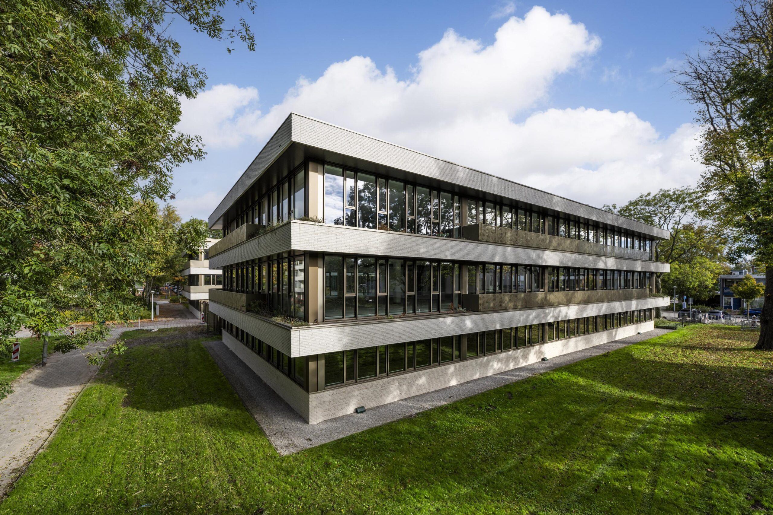 Modern three-story office building "Walborg" with large windows, surrounded by green lawn and trees under a partly cloudy sky.