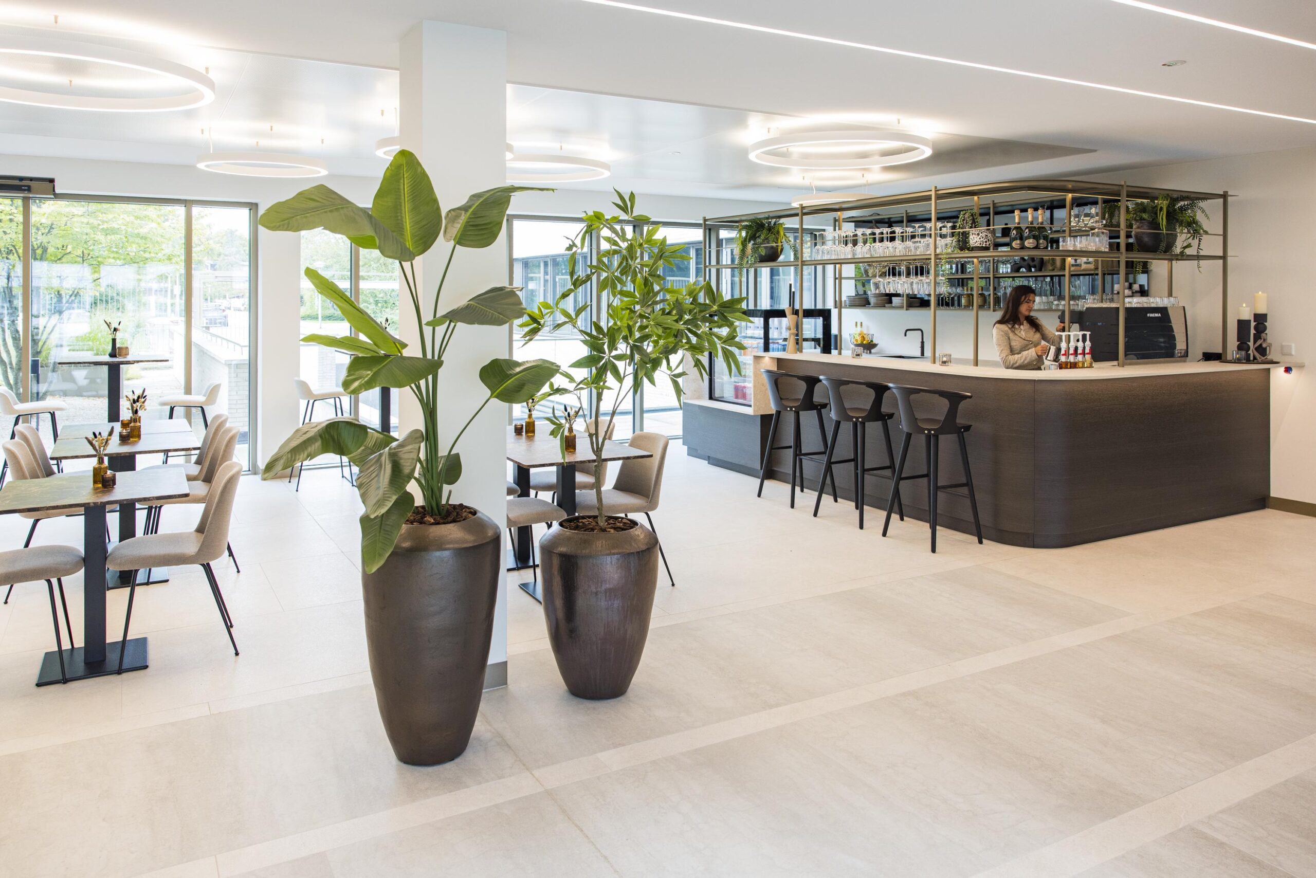 Modern and stylish hotel bar area with indoor plants, seating tables, and a bartender preparing drinks at Walborg.
