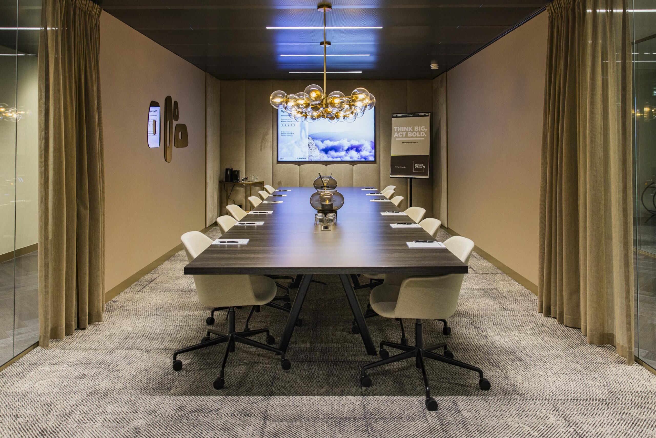 Modern conference room with a long wooden table, twelve chairs, ambient lighting, and presentation screens.