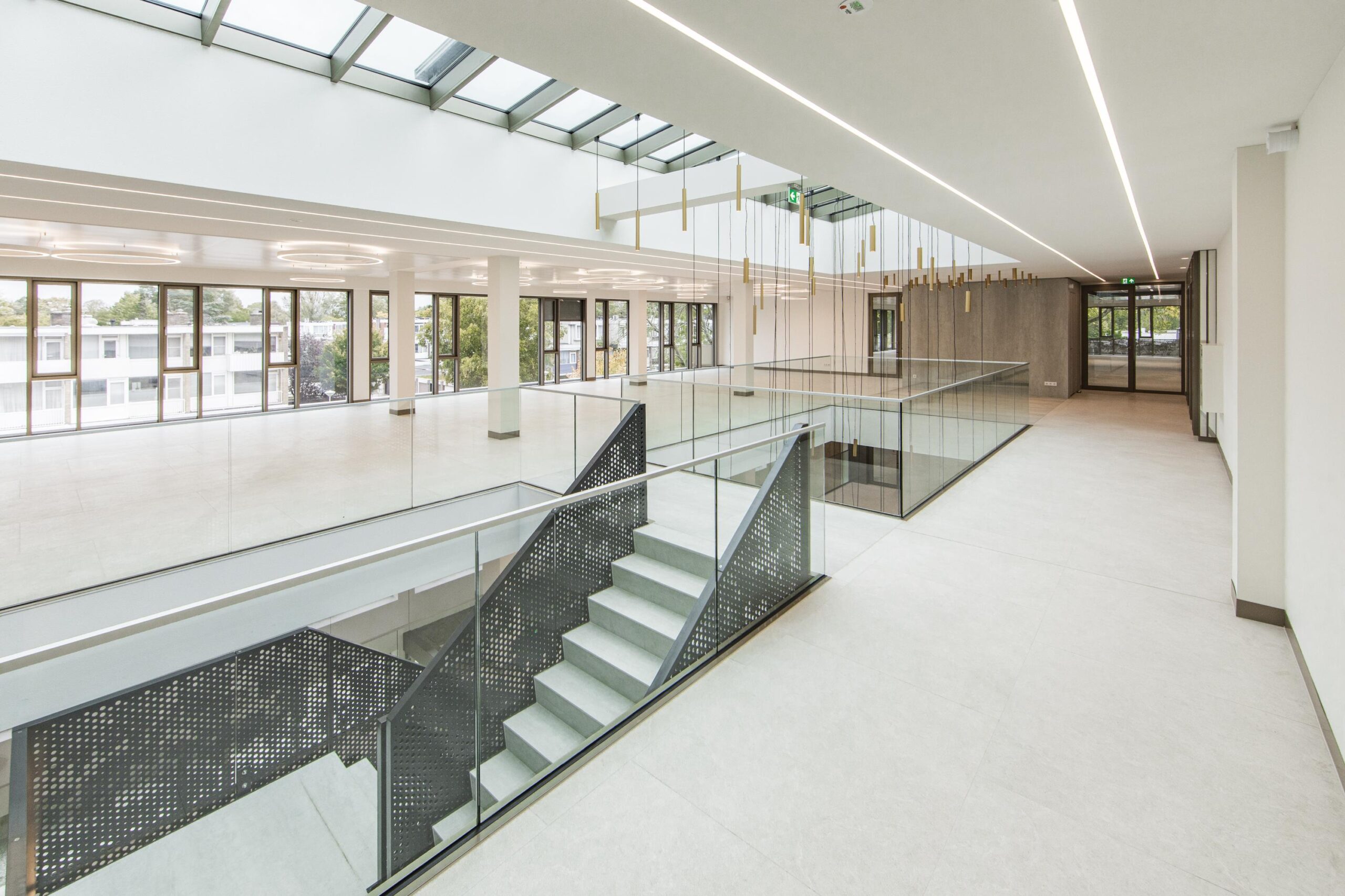 Modern, spacious atrium of the Walborg building featuring large windows, a central staircase, and a glass-railed mezzanine.