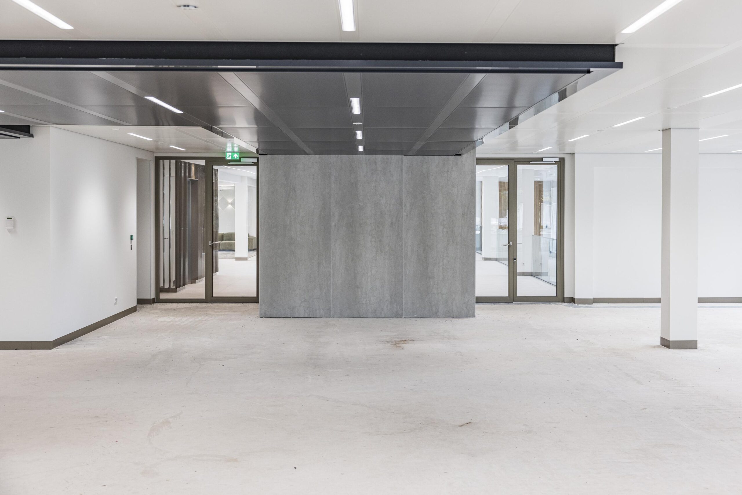 Empty modern office space with a central concrete wall and glass doors, located in the Walborg building.