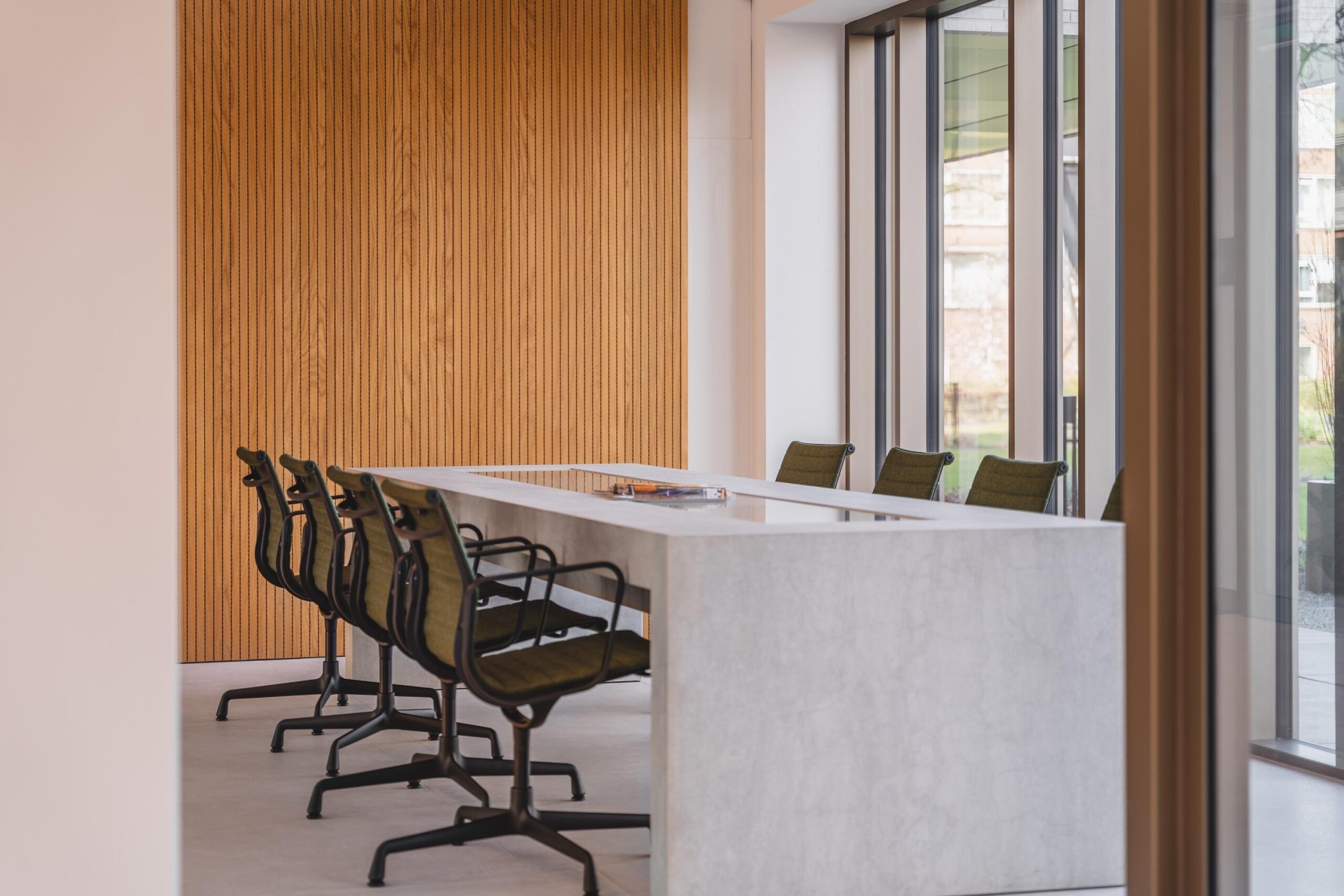 Modern conference room with a sleek concrete table, olive green chairs, and floor-to-ceiling windows.