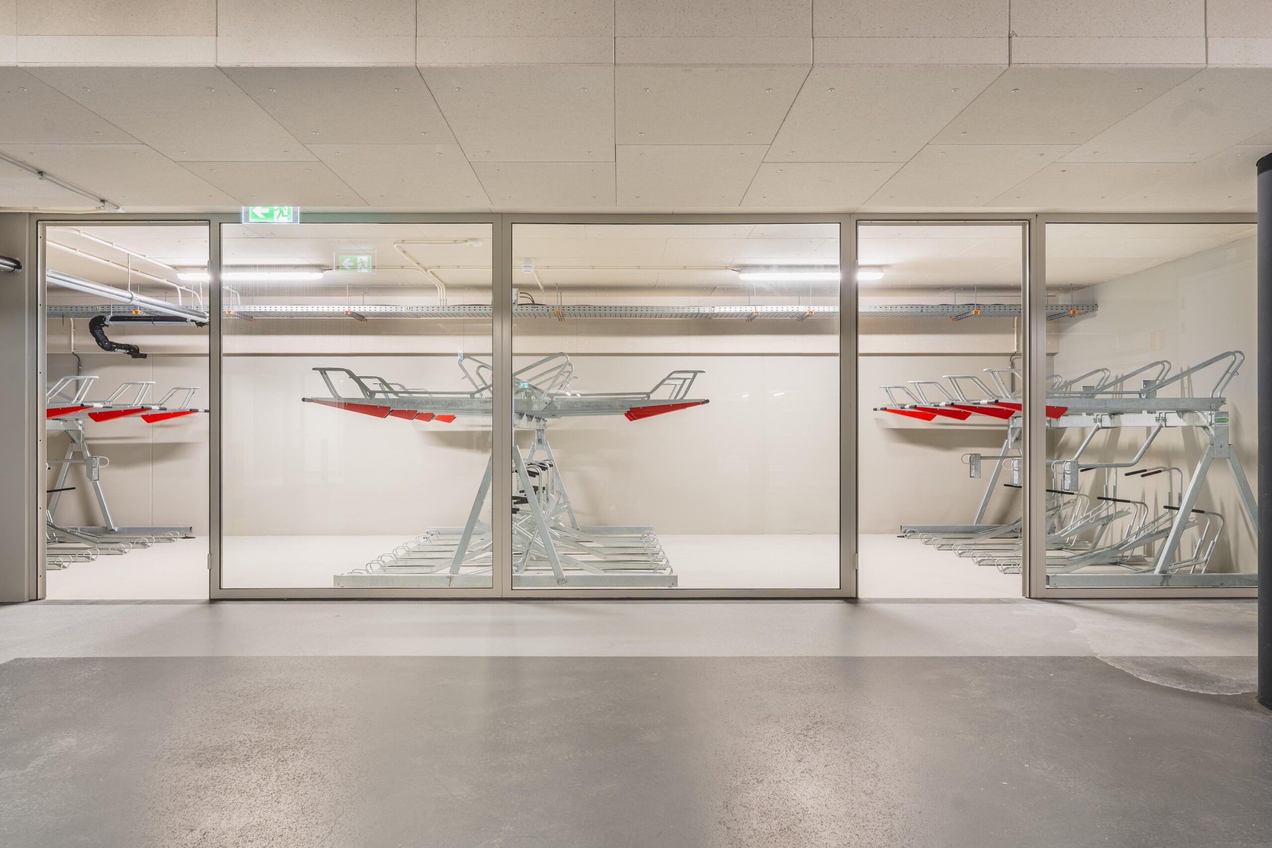 Indoor bicycle storage room with two-tier metal bike racks seen through a glass wall.