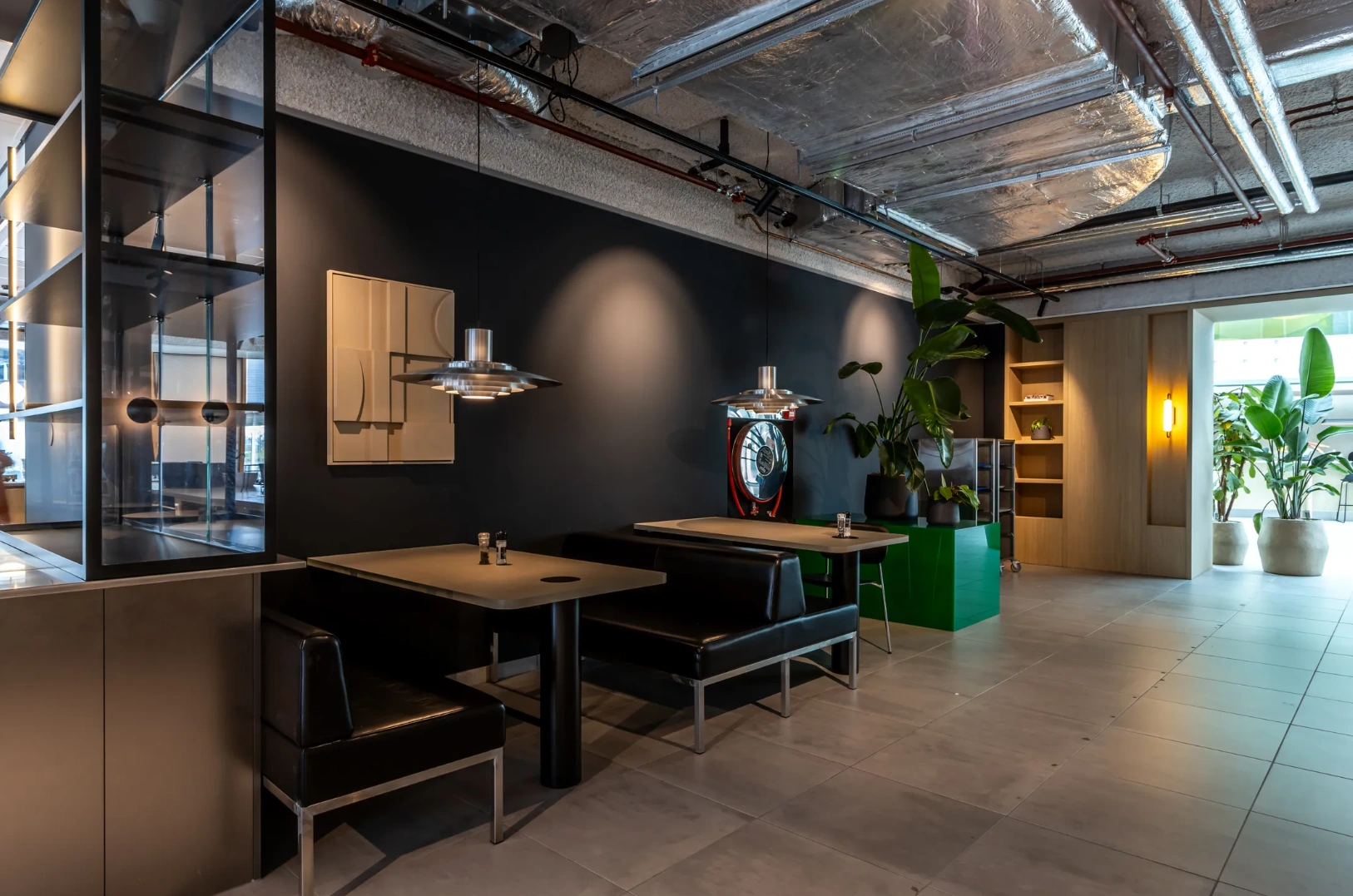 Modern seating area with black booths, industrial ceiling, and green plants at Pedro de Medinalaan.