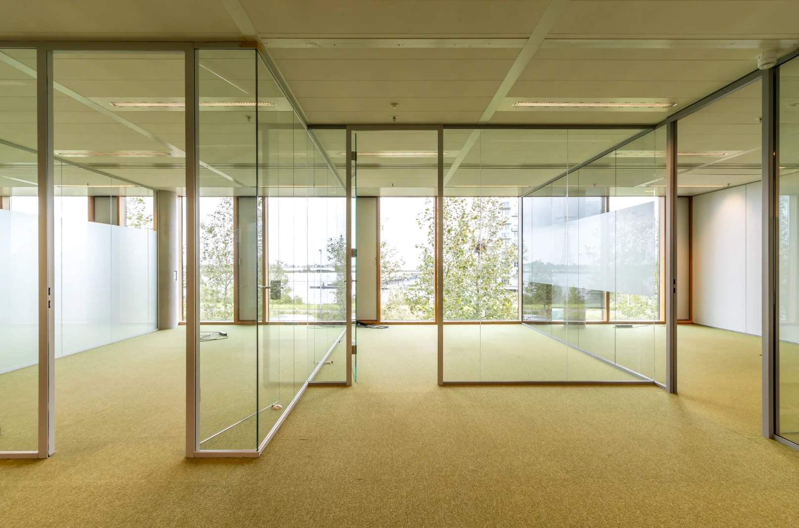 Modern empty office space on Pedro de Medinalaan with glass walls and large windows overlooking greenery and water.