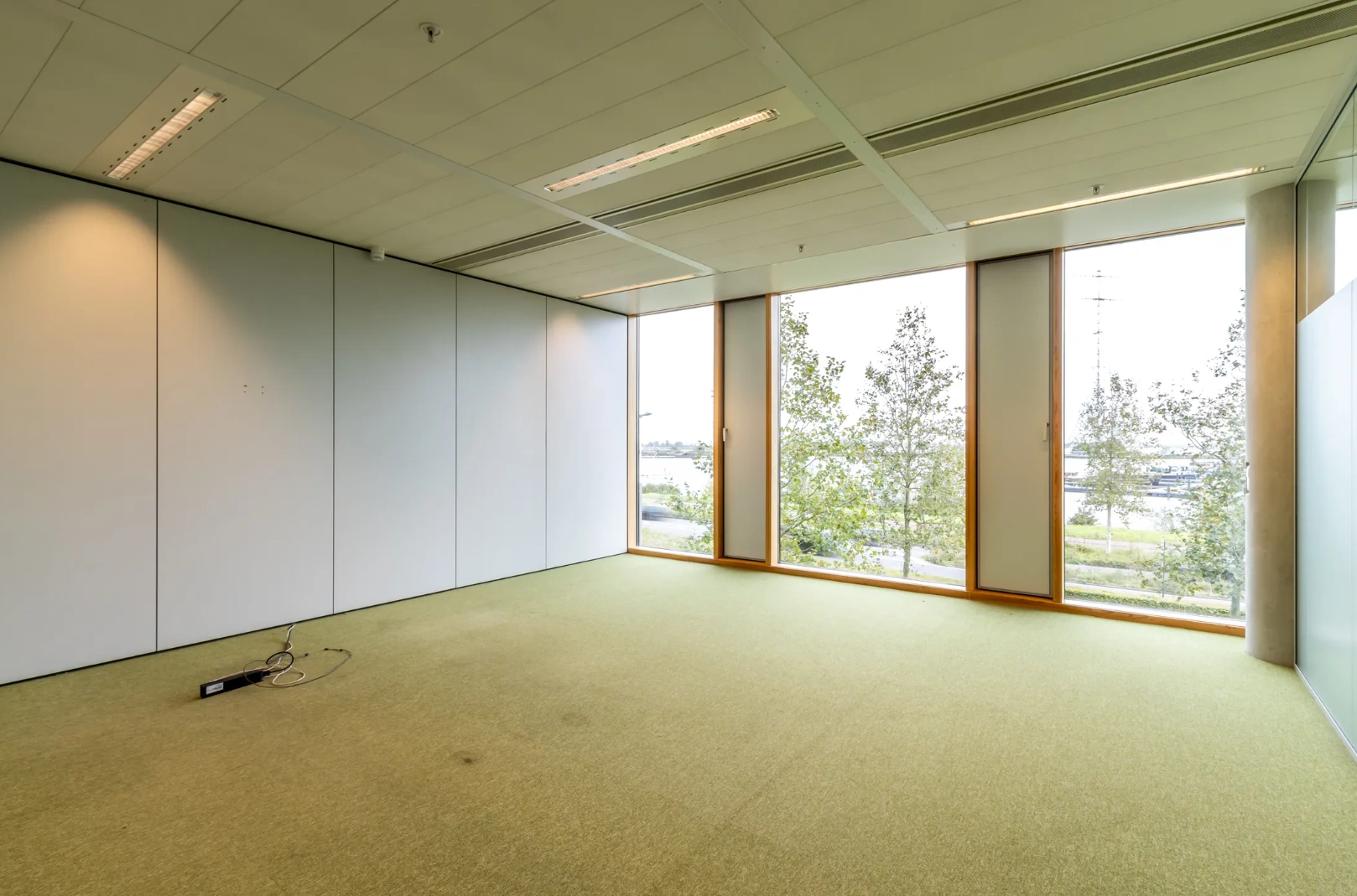 Empty office space on Pedro de Medinalaan with large windows overlooking a green area and water.