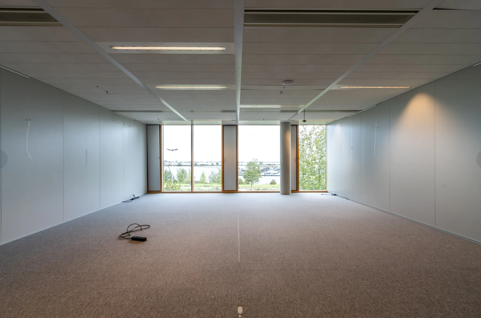 Empty office space on Pedro de Medinalaan with large windows overlooking water and a distant airport runway.