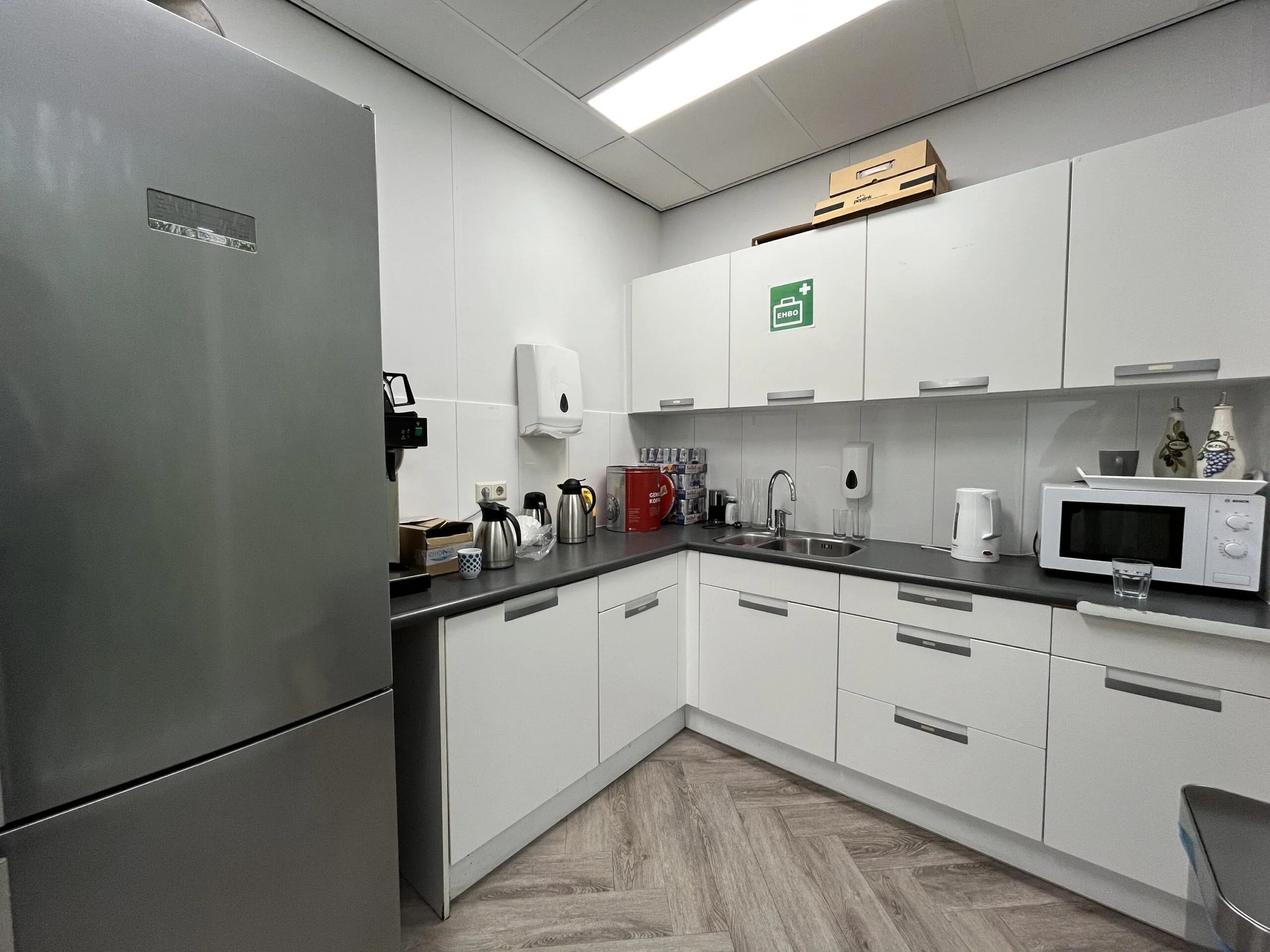 Modern office kitchen at Archimedesbaan with white cabinets, a microwave, kettle, coffee machine, and stainless steel refrigerator.