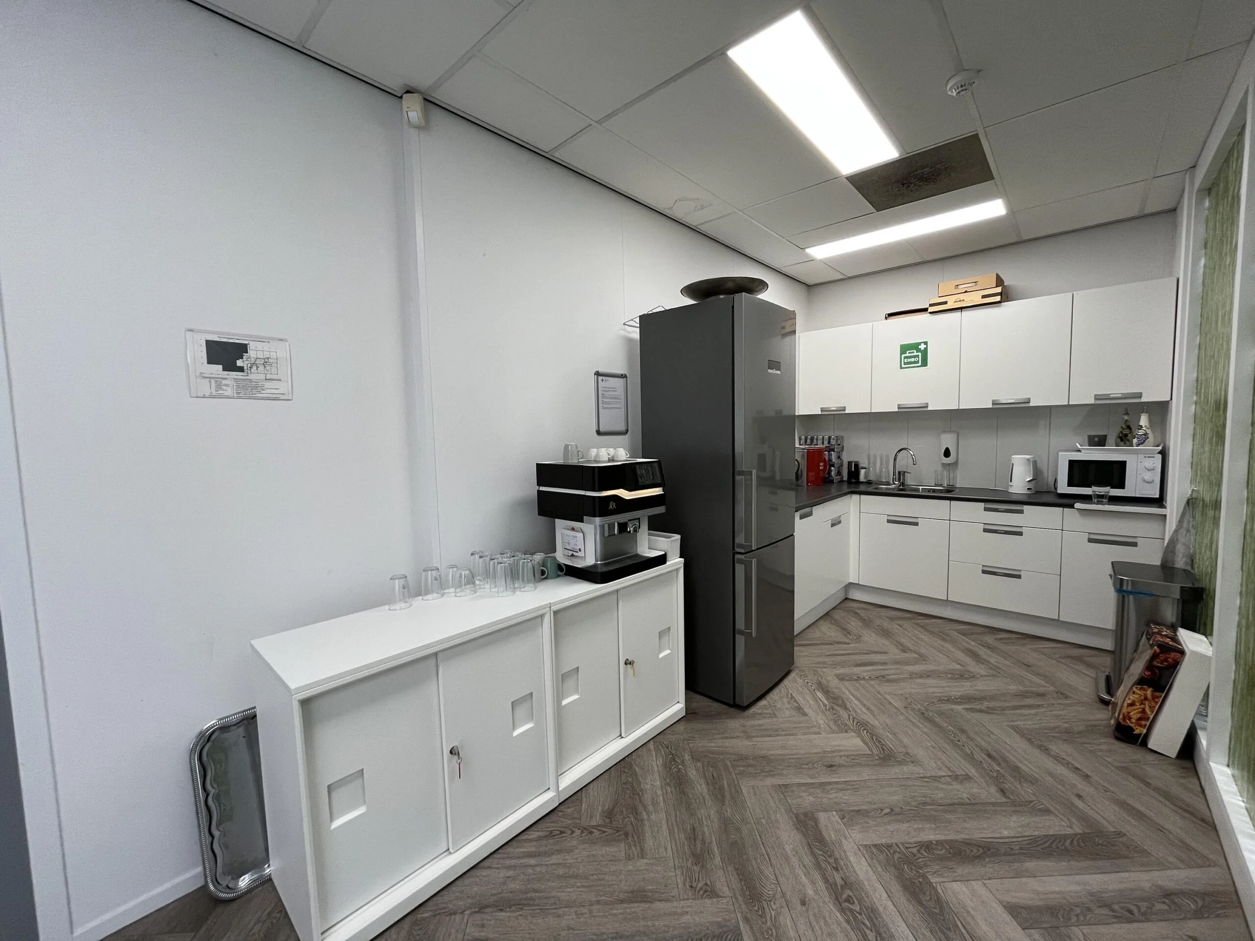 Modern office kitchen at Archimedesbaan with white cabinets, coffee machine, and various appliances.