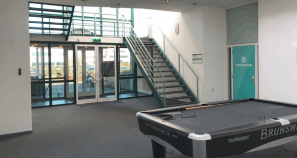 Modern office entrance with a pool table, staircase, and a glass door labeled "RapidSugar."