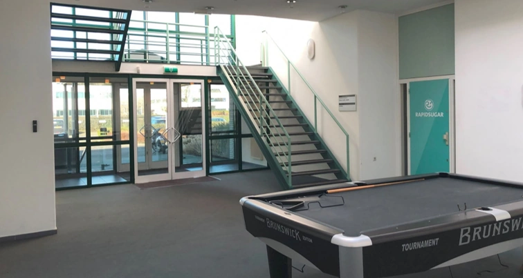 Modern office entrance with a pool table, staircase, and a glass door labeled "RapidSugar."