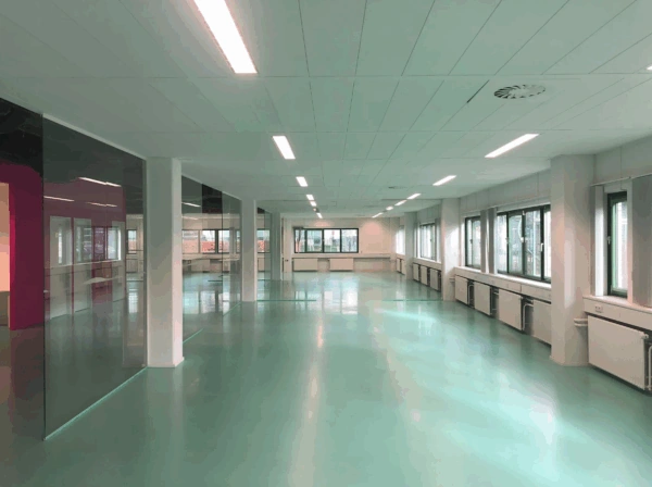 Bright, empty office space on Zekeringstraat with turquoise floor, large windows, and white ceiling panels.