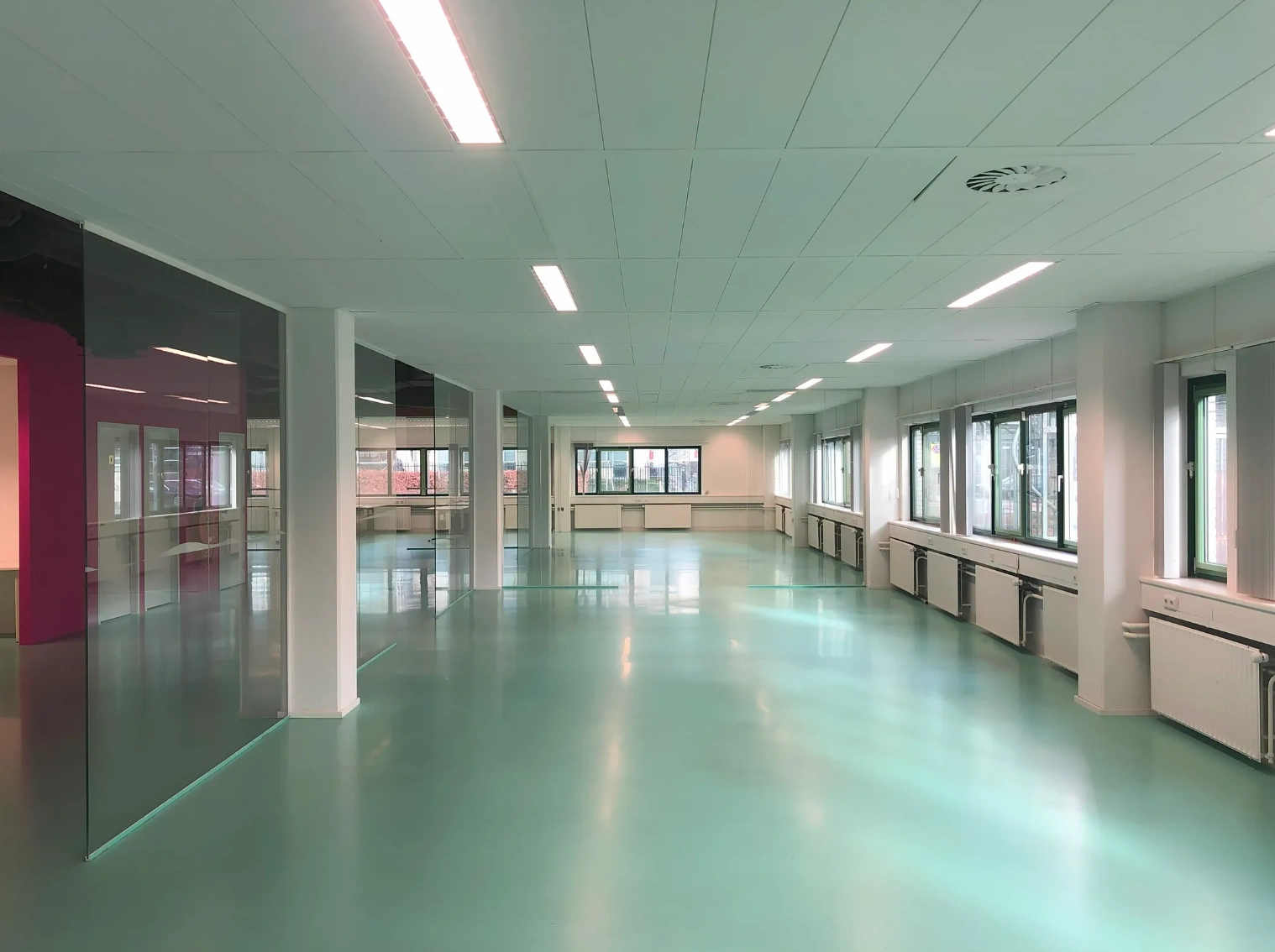 Bright, empty office space on Zekeringstraat with turquoise floor, large windows, and white ceiling panels.
