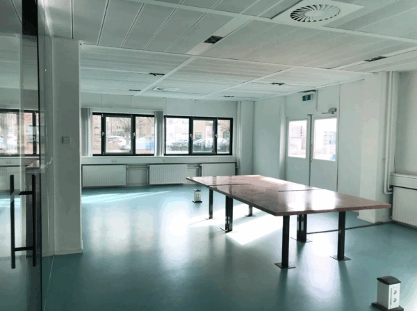 Bright, modern meeting room on Zekeringstraat with large wooden table, blue floor, and multiple windows.