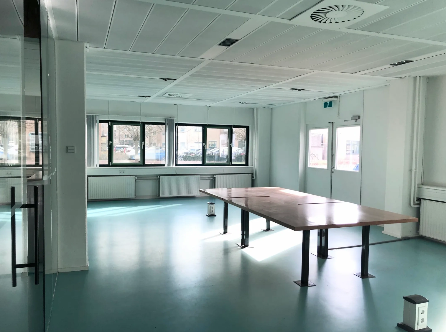 Bright, modern meeting room on Zekeringstraat with large wooden table, blue floor, and multiple windows.