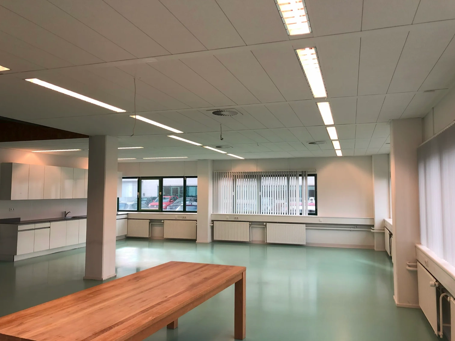 Spacious modern office kitchen and dining area with large windows and a wooden table, located on Zekeringstraat.