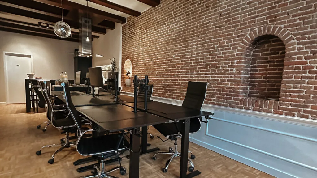 Modern office space on Herengracht with exposed brick walls, black desks, and ergonomic chairs.