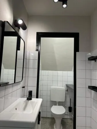 Modern, compact bathroom on Herengracht with white tiles, a toilet, sink, and minimalist black fixtures.